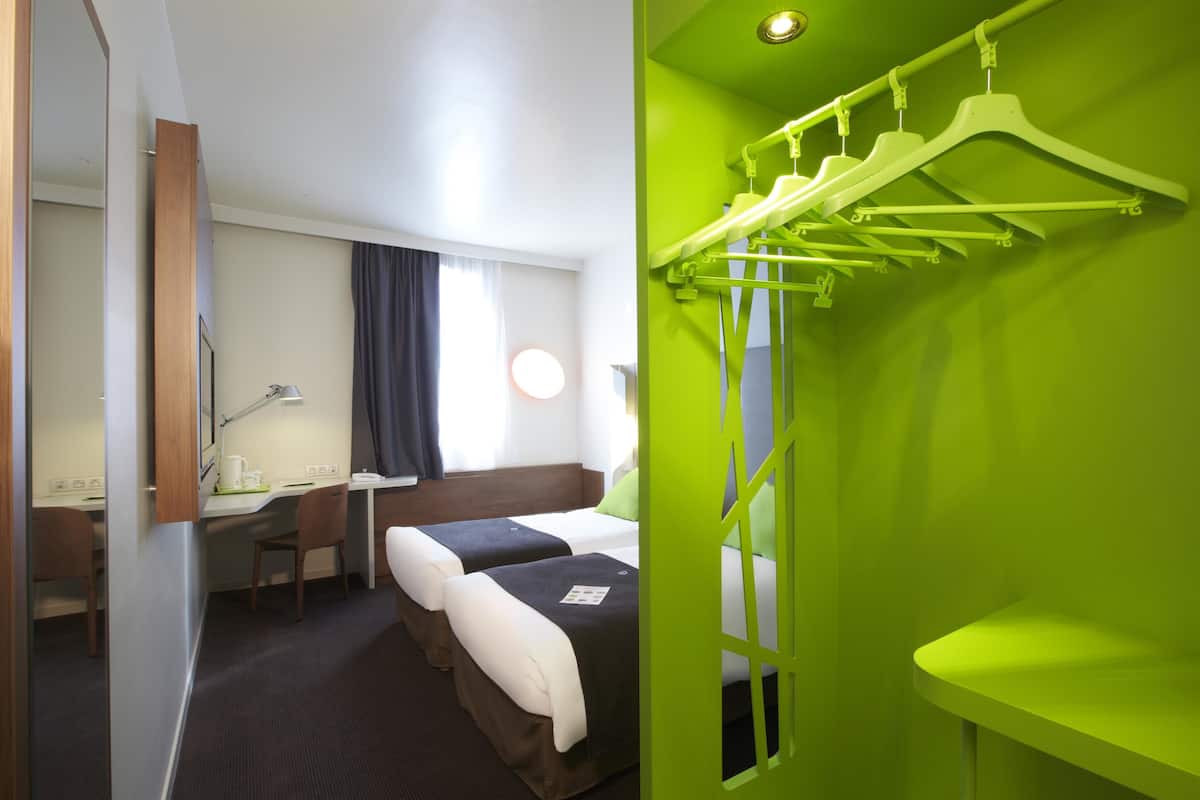 Une chambre d’hôtel avec deux lits, un bureau, une chaise et un mur vert sur lequel est fixé un étendoir à linge.
