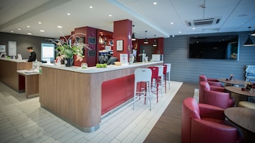 Una moderna zona de recepción con mostrador de madera, taburetes de bar rojo y blanco, y un área de descanso con sillas y mesas rojas.