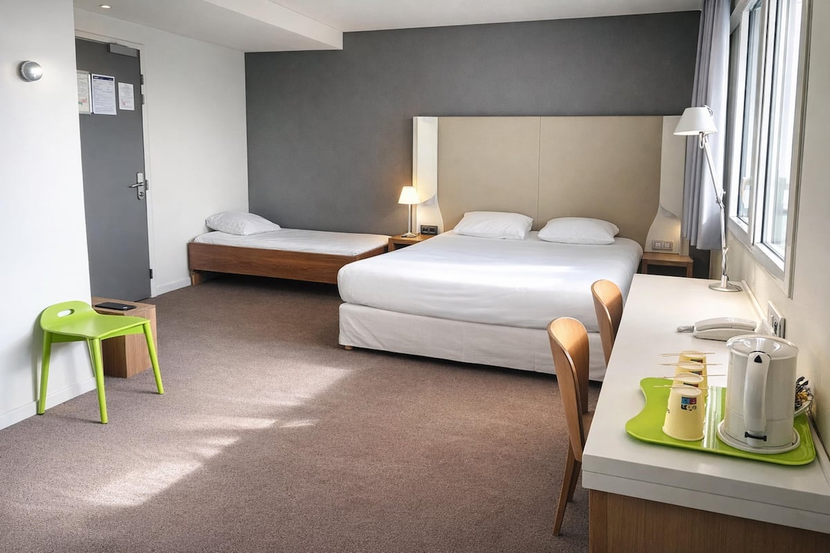 Une chambre d’hôtel avec deux lits, un bureau avec une lampe, une chaise et une machine à café.