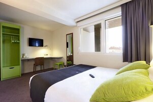 A hotel room with a bed, a desk, a chair, a television, and a wardrobe.