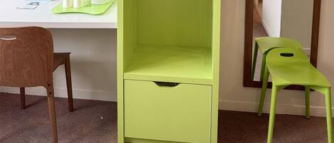 A room with a green wardrobe, a desk with a computer, a chair, and a mirror.