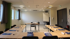 Une salle de conférence équipée de longues tables, de chaises, d’un tableau blanc et d’un extincteur.