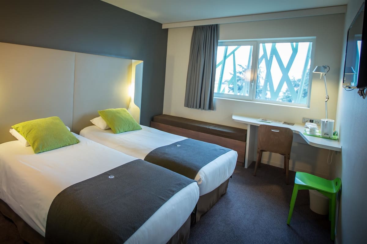 Une chambre d’hôtel avec deux lits, un bureau, une chaise et une fenêtre donnant sur un paysage agréable.
