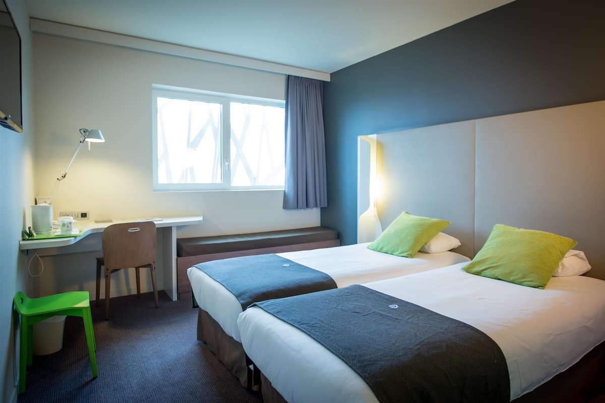 A hotel room with two beds, a desk, a chair, and a window with curtains.