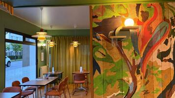 A room with a dining area, chairs, tables, and a large abstract painting on the wall.