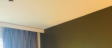 Habitación de hotel con dos camas individuales, un ventanal con cortinas, una lámpara de pared y una lámpara en el techo.