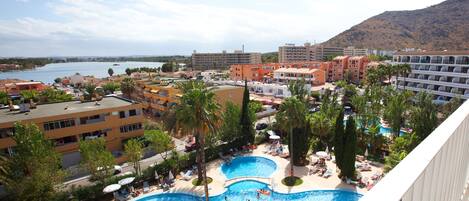 A resort with two swimming pools, palm trees, and a view of the sea.