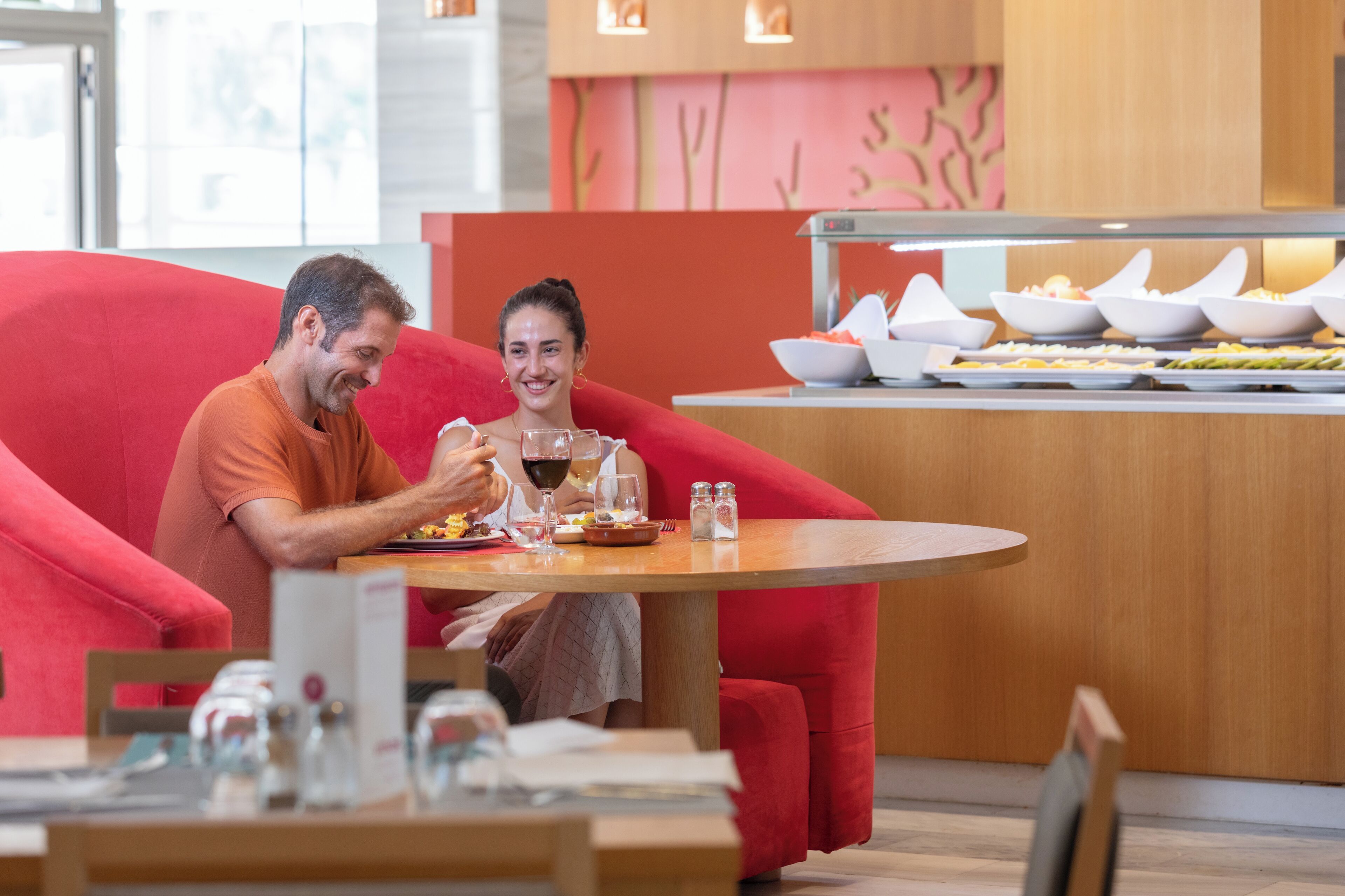 Una pareja cenando en una mesa con una silla roja, un bufé con diversos platos y una decoración de interiores moderna.