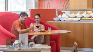 Una pareja cenando en una mesa con una silla roja, un bufé con diversos platos y una decoración de interiores moderna.