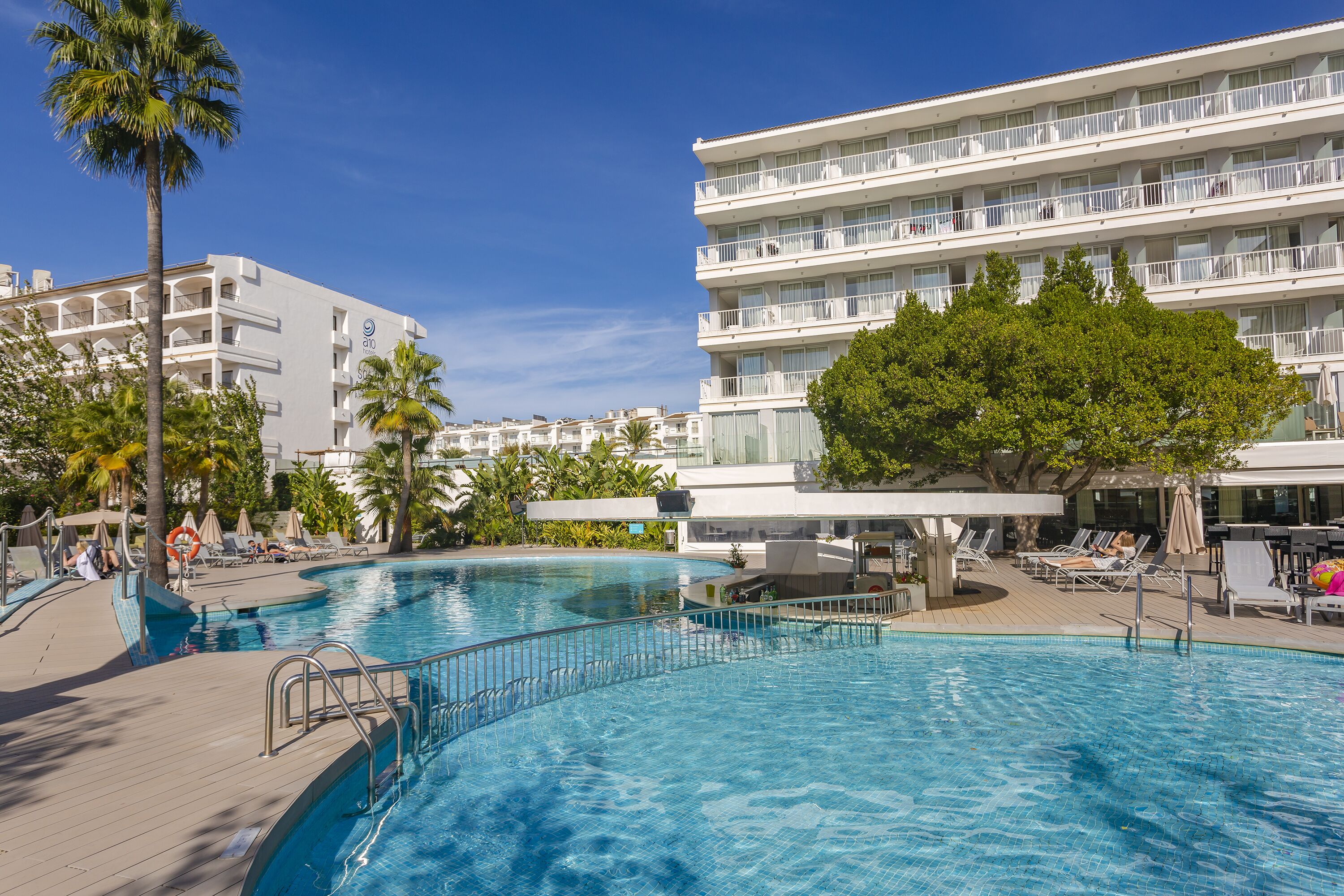 Un hotel con una piscina grande, varios balcones y palmeras.