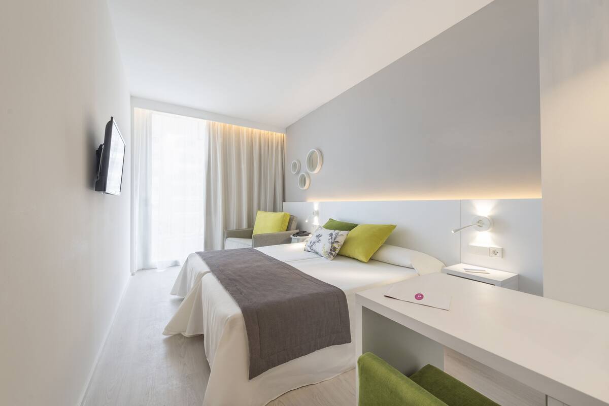 A modern hotel room with a bed, bedside table, and a desk with a chair.