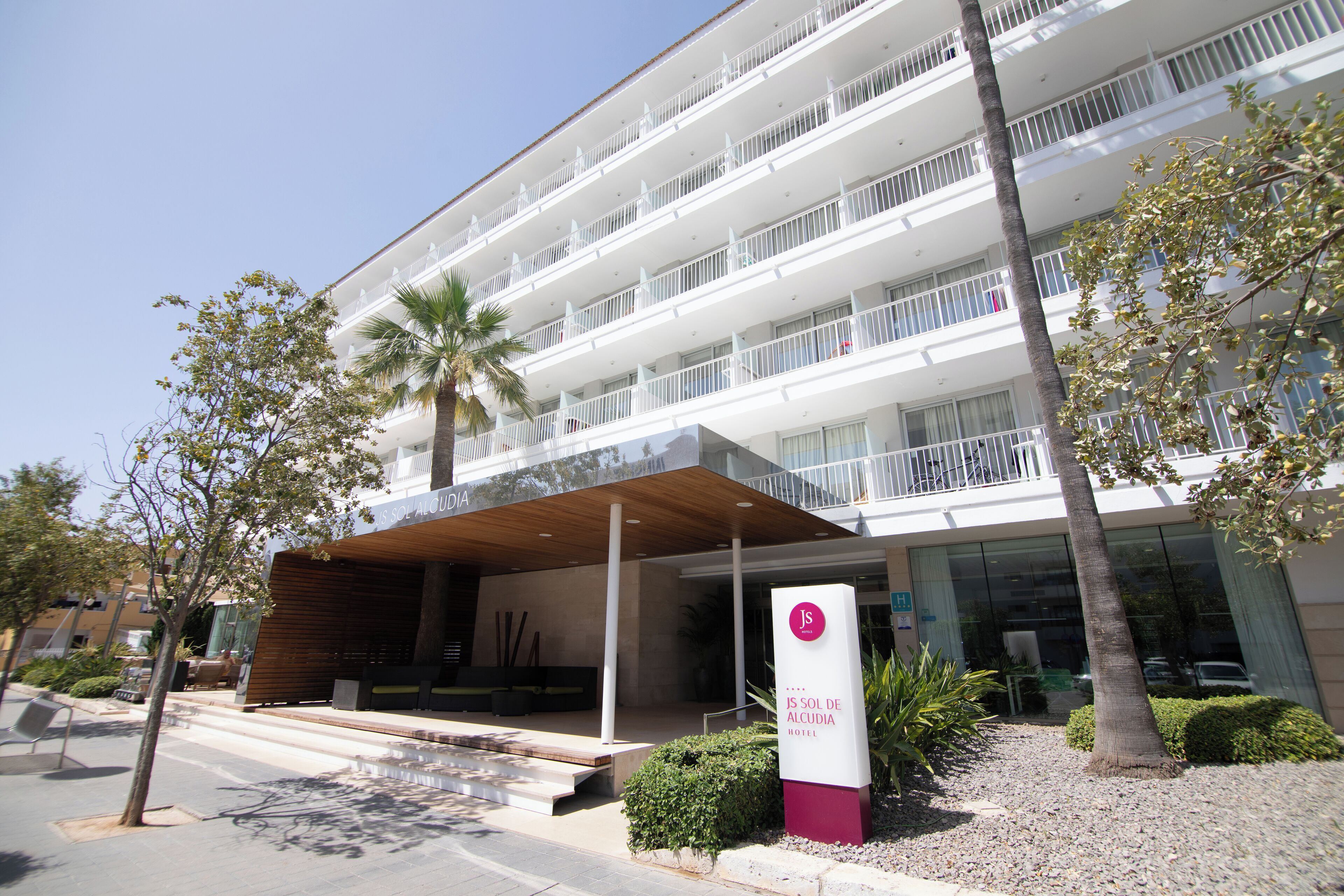A multi-story hotel with a modern design, featuring balconies on each floor, a covered entrance, and a sign indicating the hotel name.