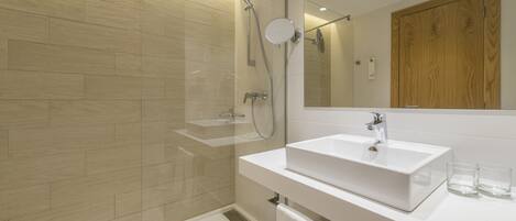 A modern bathroom with a glass shower enclosure, a white sink, and a wooden door.