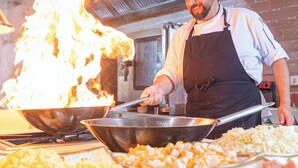 A chef cooking with a large wok on a stove, surrounded by various food items. - Hotel JS Sol de Alcudia (Alcúdia)