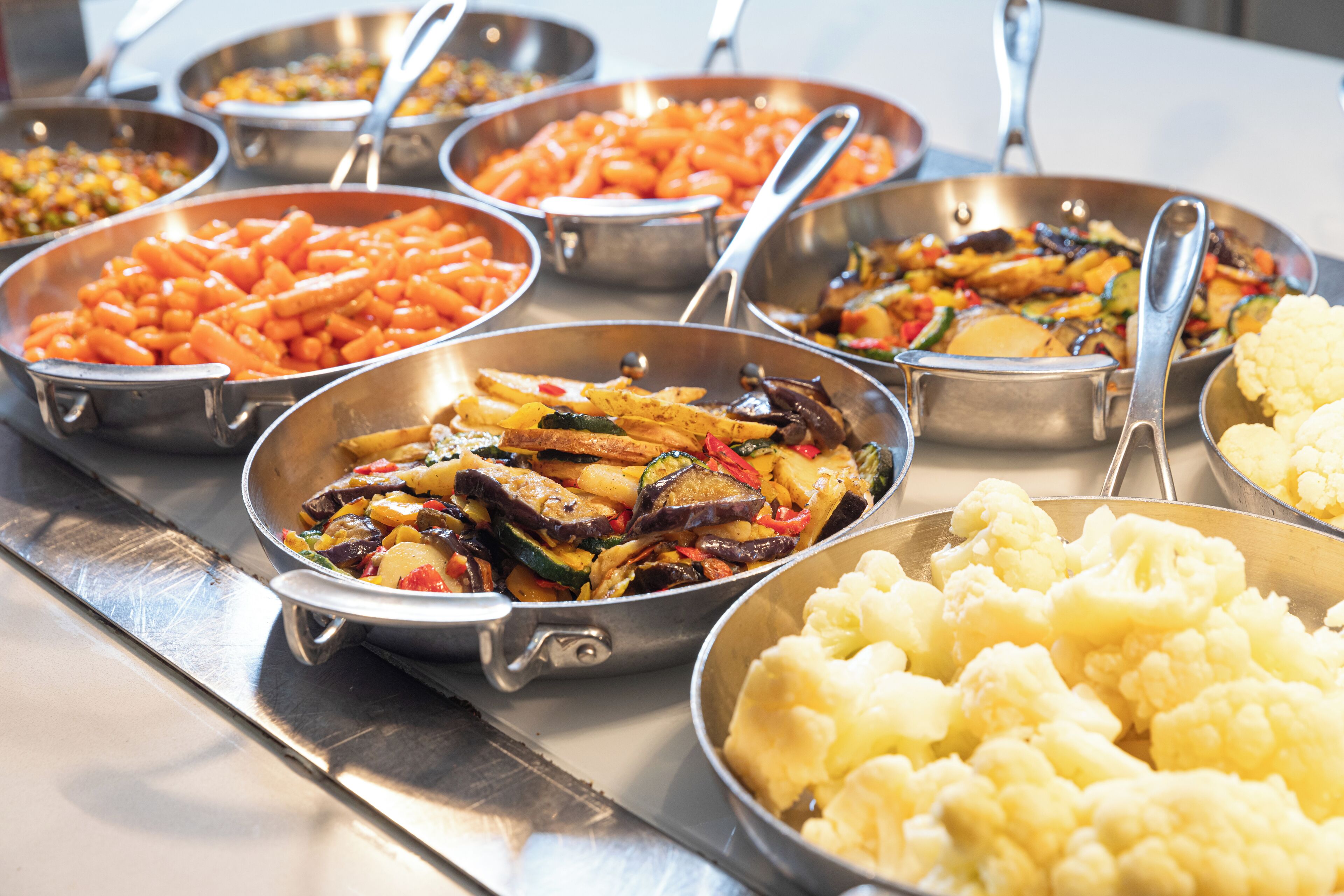 Un bufé con diversos platos, incluyendo zanahorias, coliflor y verduras variadas.