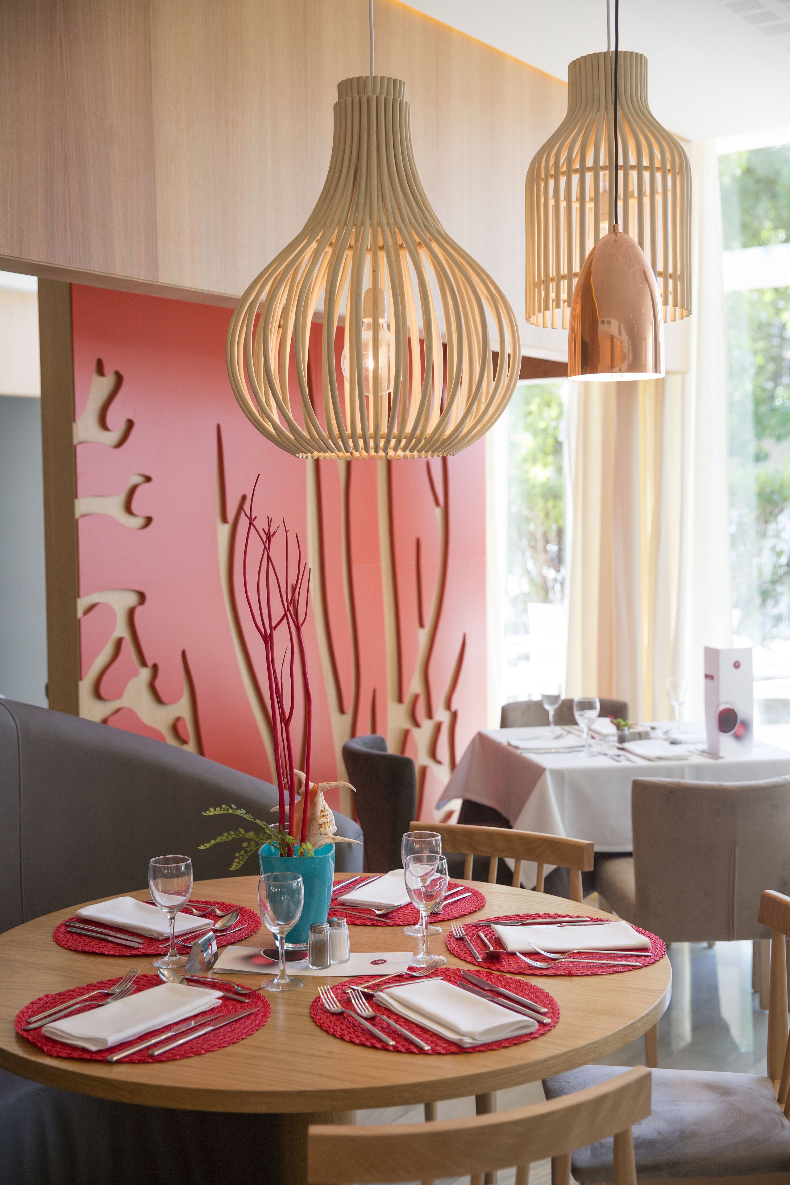 A dining area with a round wooden table set for two, red placemats, and a vase with branches.