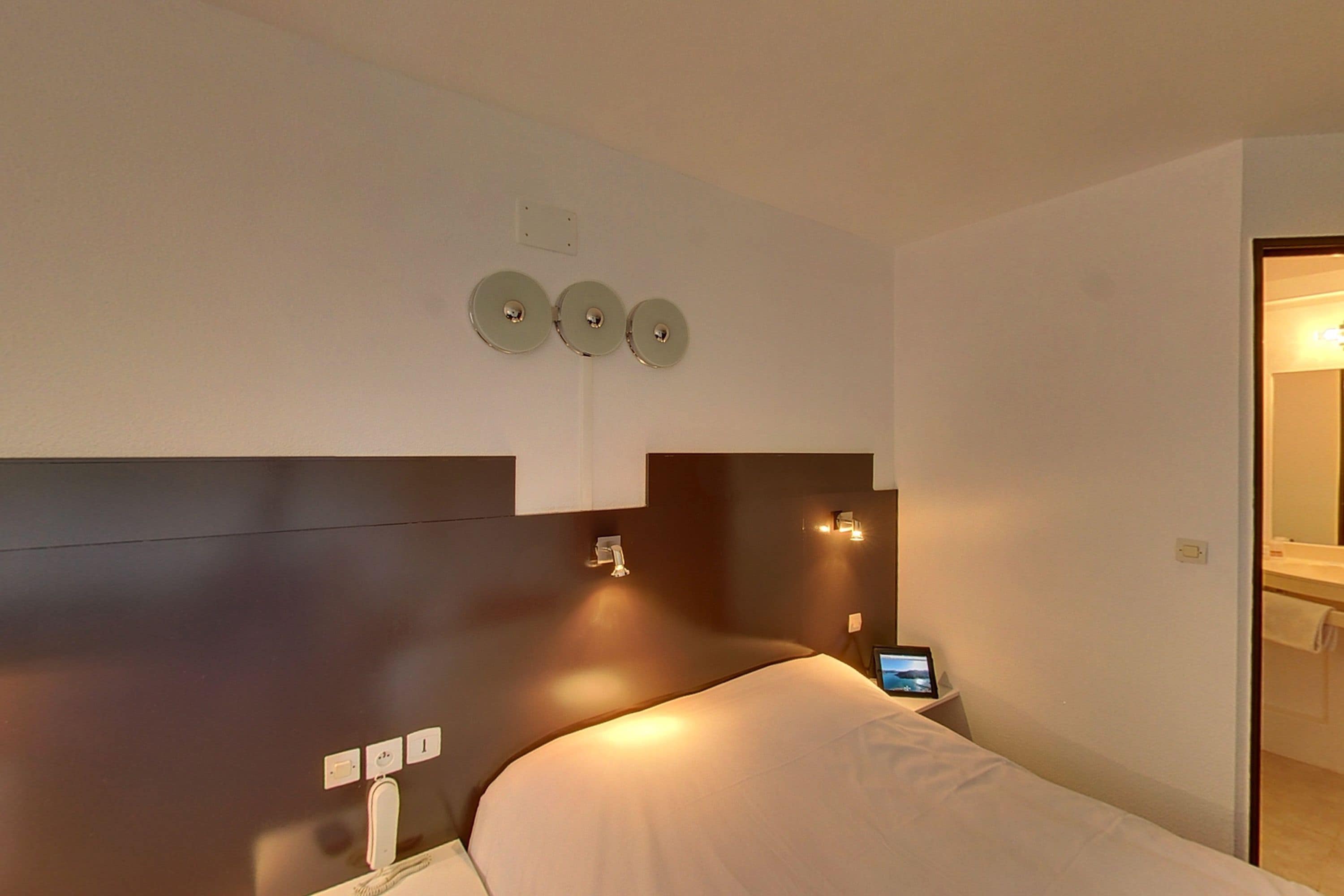 Une chambre d’hôtel moderne équipée d’un lit, d’une table de chevet et d’appliques murales.