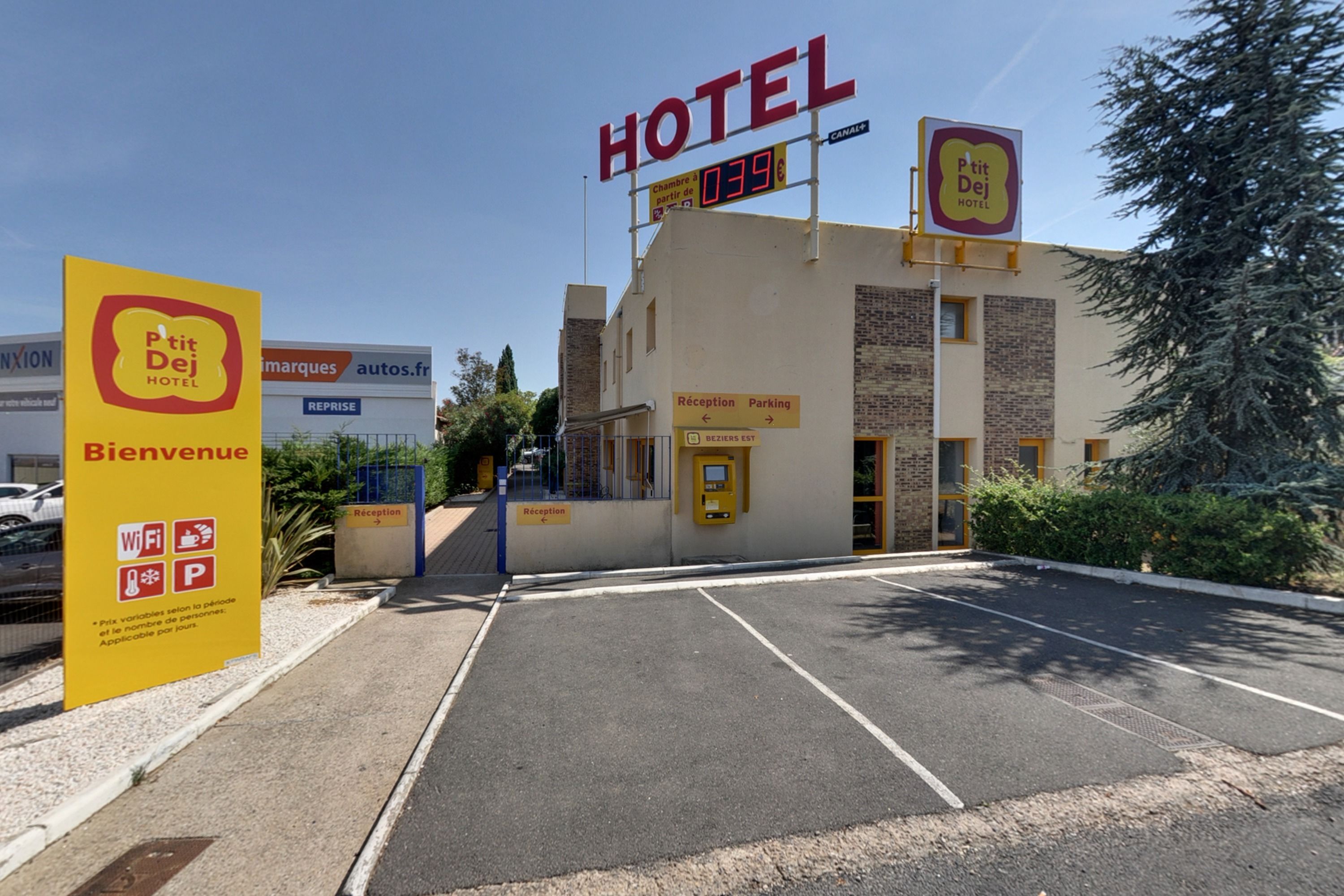 Entrada de um hotel com balcão de recepção, placa de estacionamento e sinal de boas-vindas.