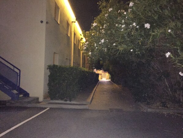 A narrow alleyway with a staircase leading up to a building, surrounded by greenery and illuminated by artificial lighting.