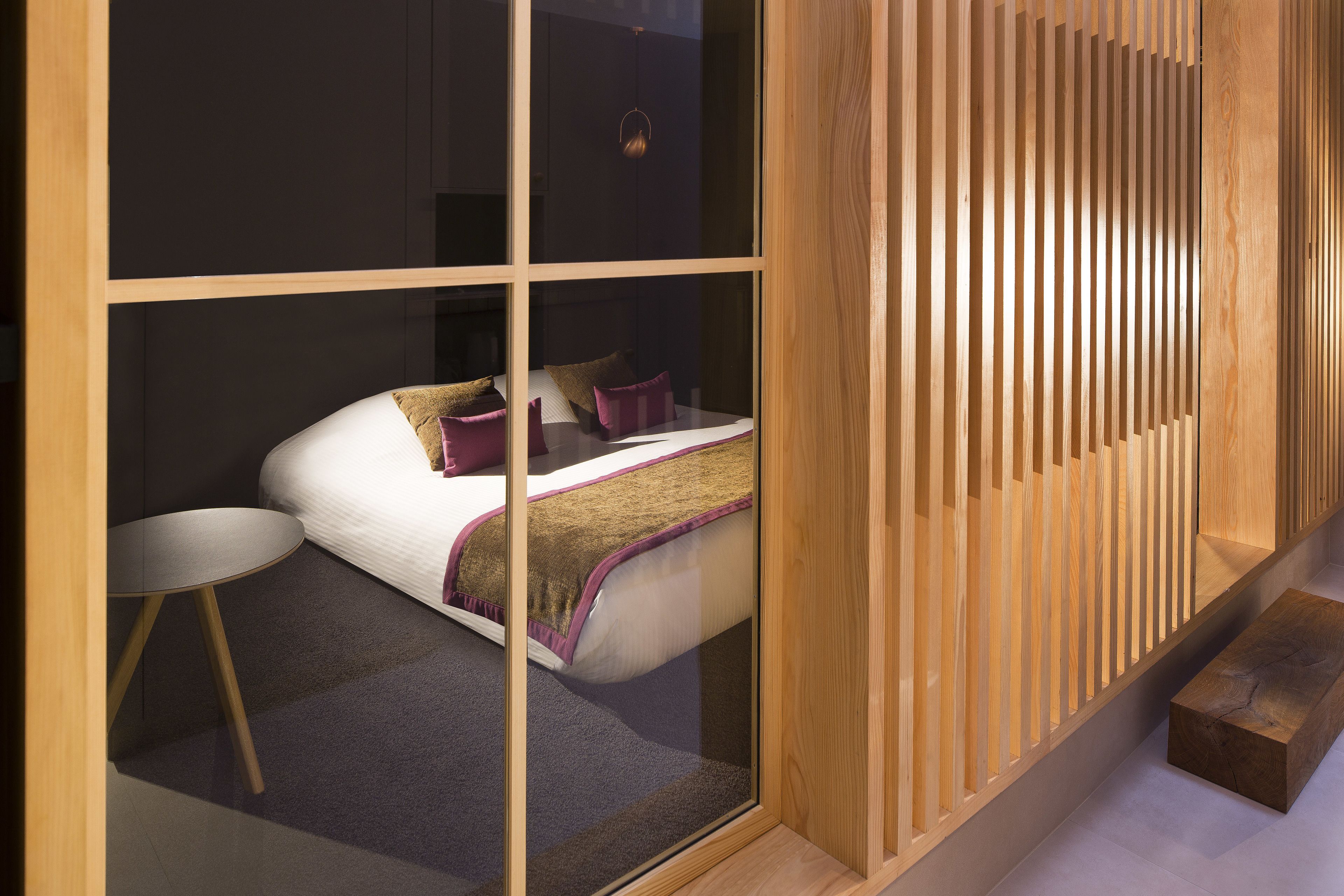 Un dormitorio moderno con una cama, una mesita redonda pequeña y un banco de madera.
