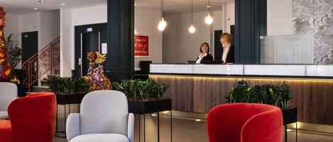 A lobby with red and grey chairs, a reception desk, and hanging wicker lamps.
