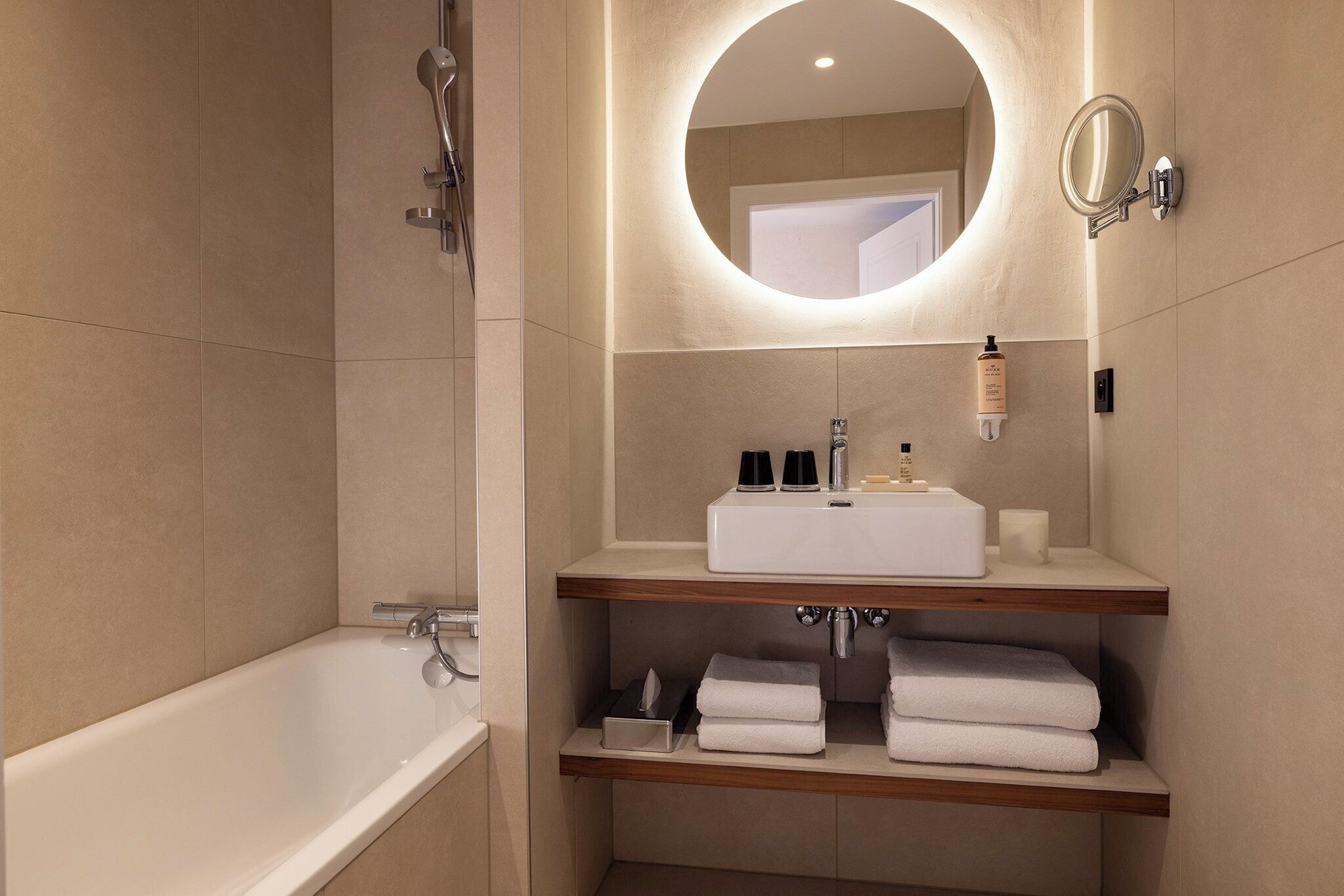 A modern bathroom with a bathtub, a vanity with a mirror, and shelves with towels.