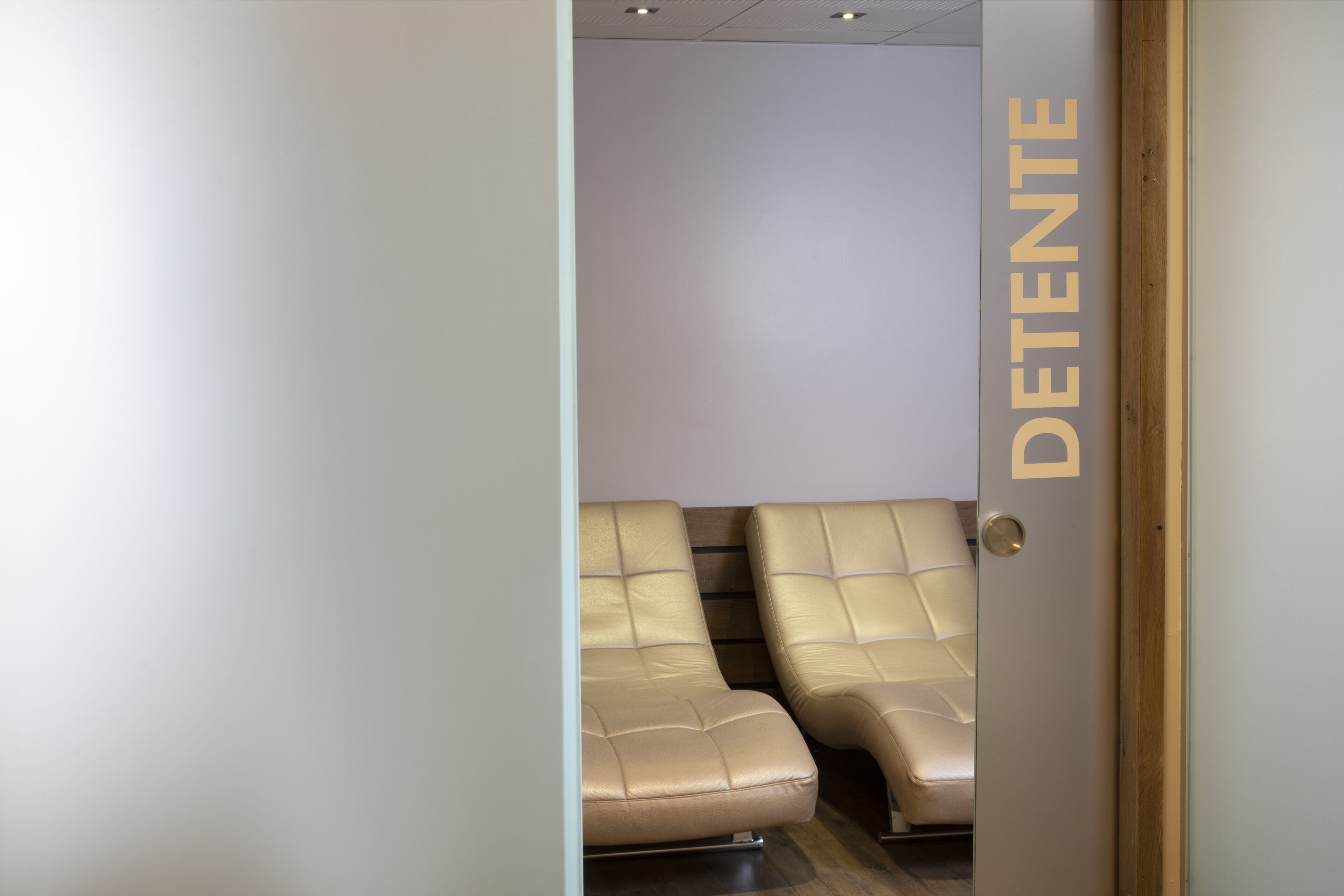 A room with two beige leather chairs and a door with the word "DETENTE" on it.