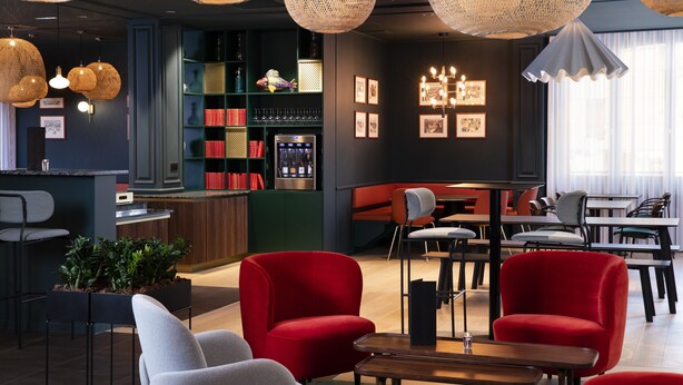 Zona de bar moderna con lámparas colgantes de mimbre, sillas rojas y grises, y una barra con minibar.