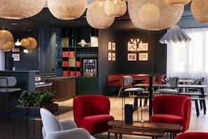 A modern bar area with wicker pendant lighting, red and grey chairs, and a bar counter with a minibar. - Hôtel Le Colombier (Obernai)