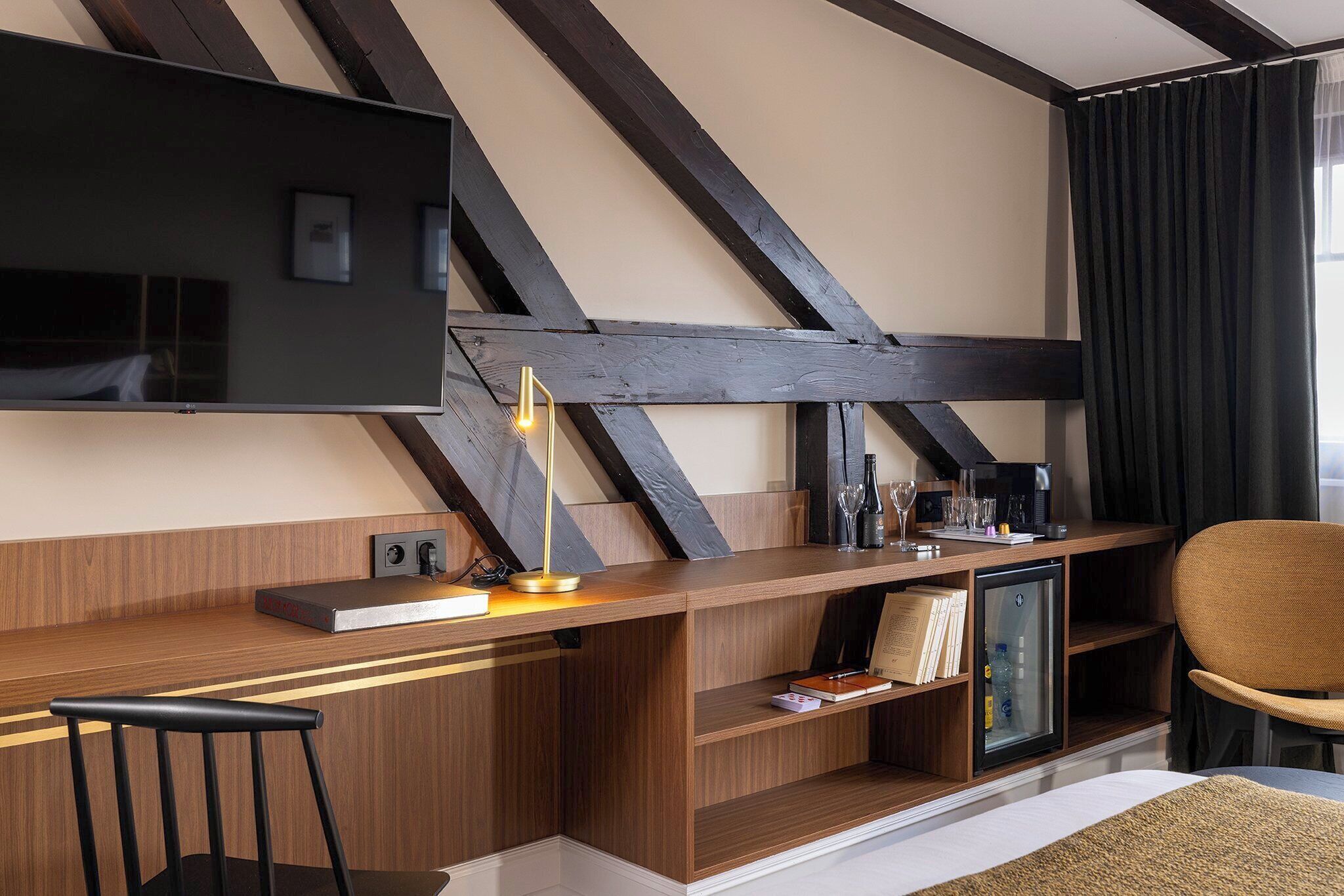 Habitación de hotel moderna con un escritorio de madera, un televisor de pantalla plana, un refrigerador pequeño y una silla cómoda.