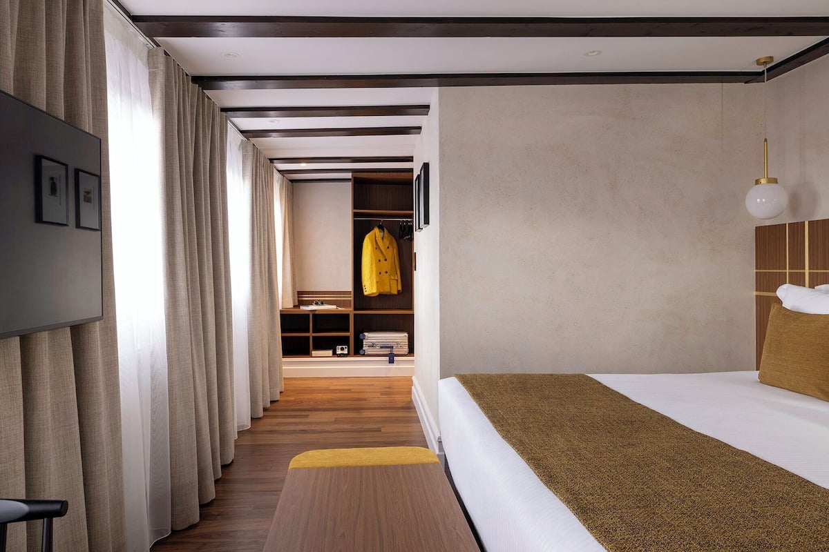 Ein Hotelzimmer mit Bett, Kleiderschrank, Spiegel und einem fenster mit Vorhängen.