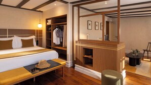 Una habitación de hotel con una cama grande, un tocador de madera, un banco y un espejo.