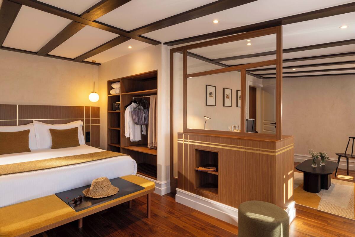 Ein Hotelzimmer mit einem großen Bett, einem Holznähtischchen, einer Bank und einem Spiegel.