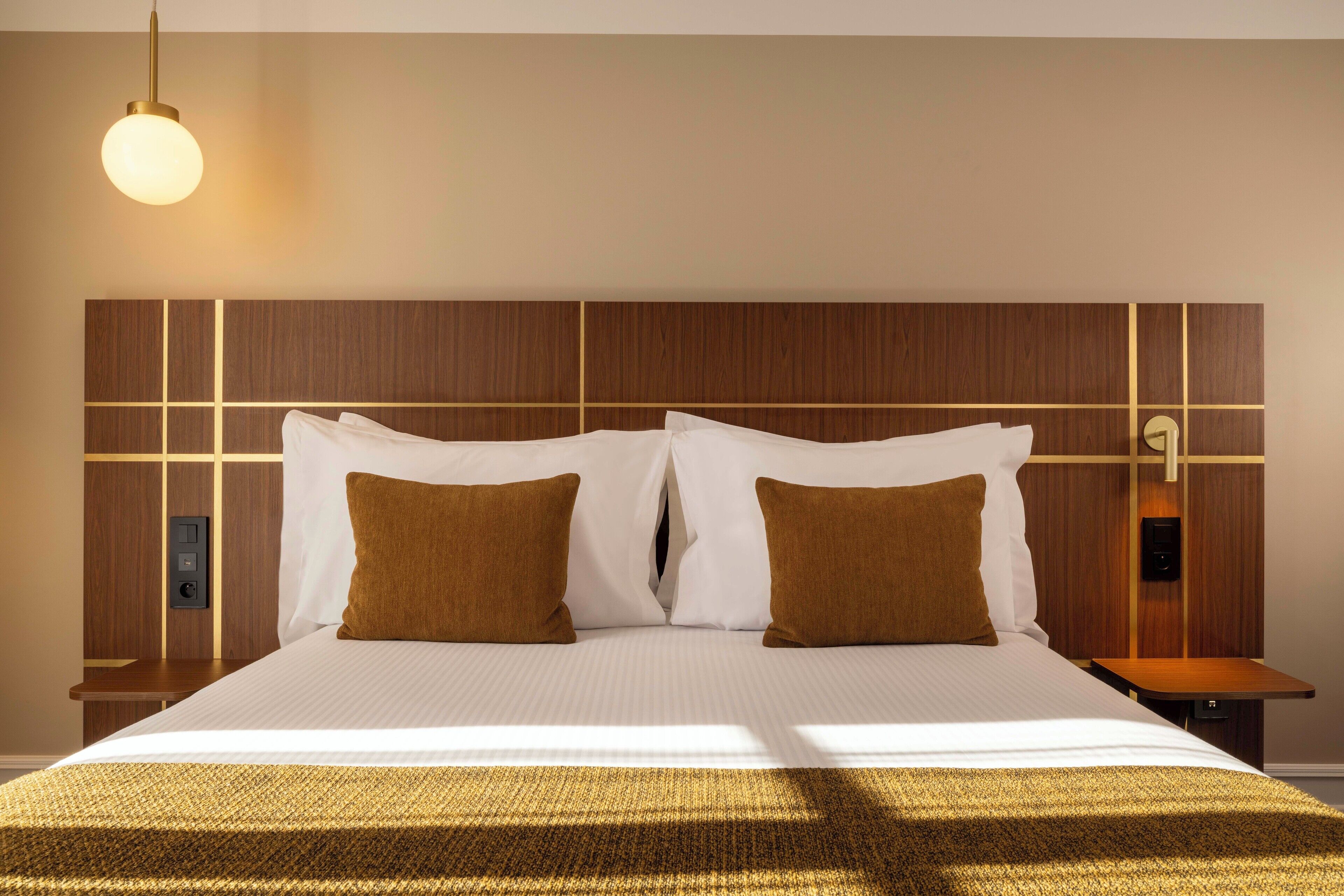 Habitació d'hotel amb un llit gran, dos coixins, una taula de nit i una làmpada fixa a la paret.