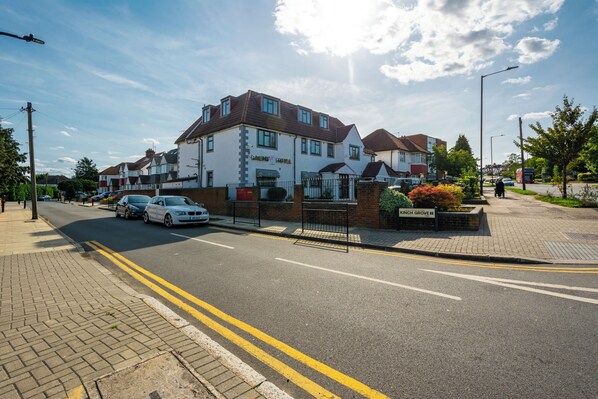 A residential building with a gated entrance, a driveway, and a street with parked cars. - The Brent Hotel  (Harrow)