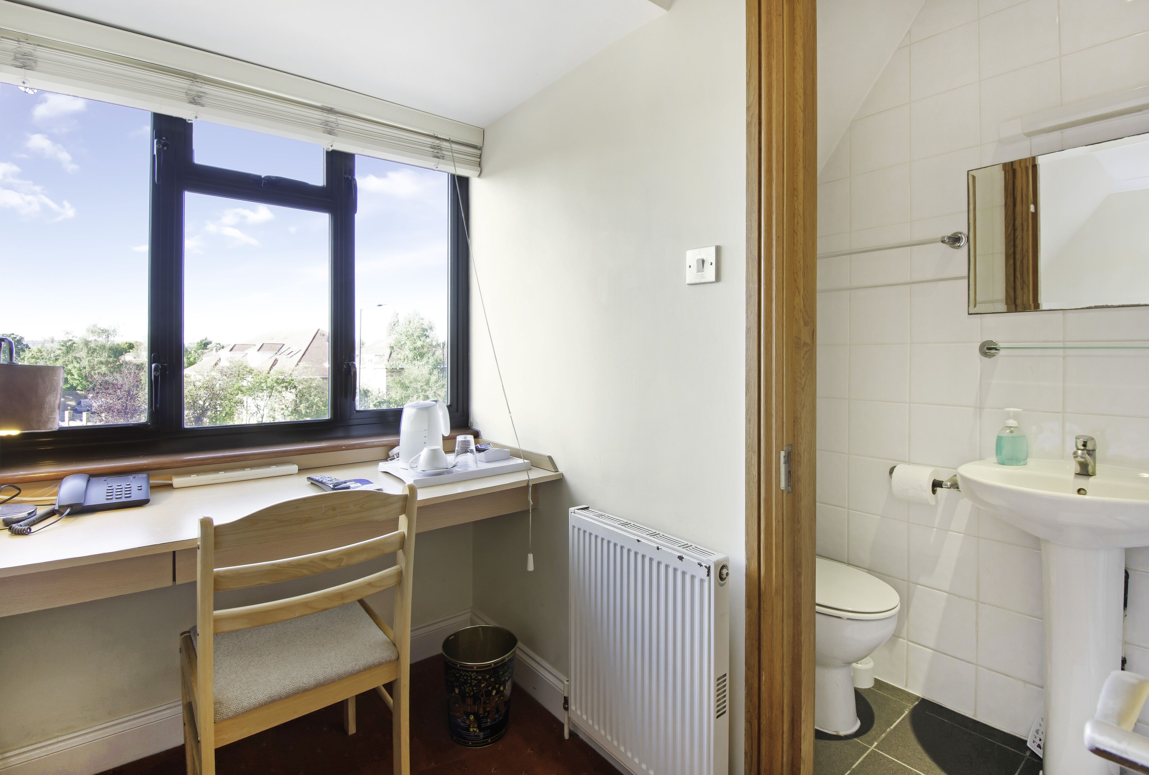 A room with a desk, chair, radiator, toilet, and a window with blinds.