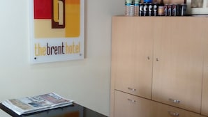 En hotellobby med en receptionsdisk, en inramad skylt med texten ”The Brent Hotel” och ett skåp med diverse föremål ovanpå.