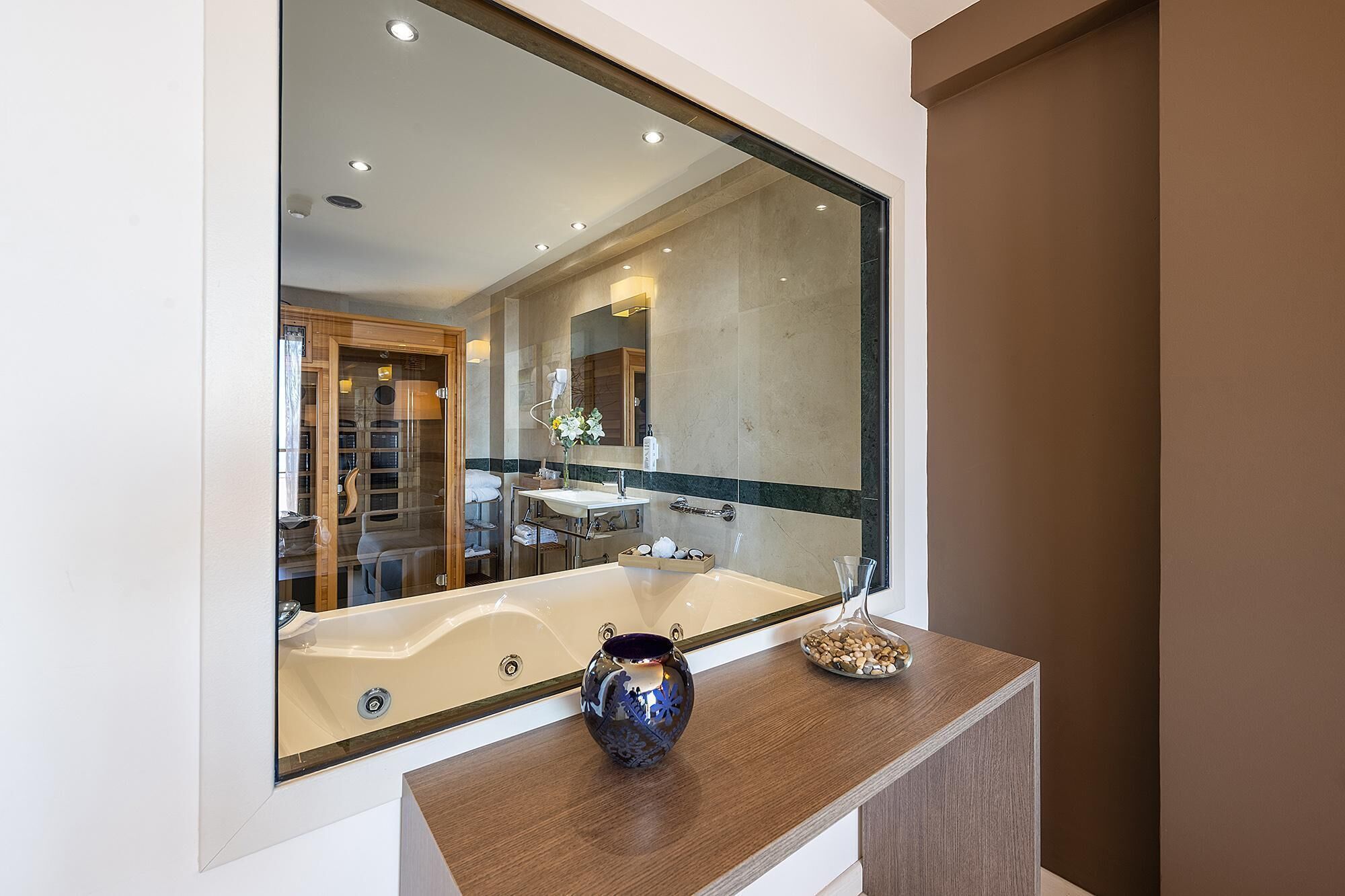 A modern bathroom with a large mirror, a bathtub, a wooden vanity, and a glass vase on the counter.