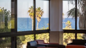 A room with large windows overlooking a coastal area with palm trees and the sea.