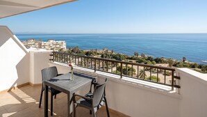 A balcony with a table and chairs, overlooking a coastal view with buildings and palm trees.