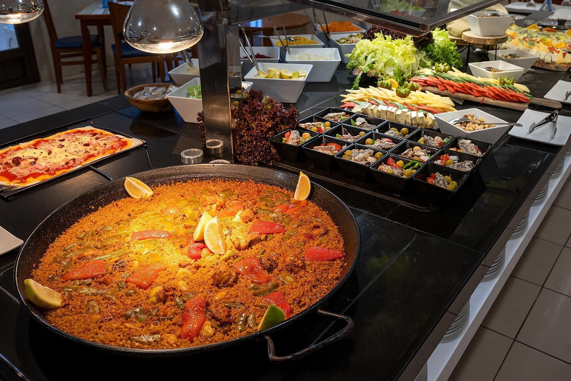 A buffet with a large pot of rice, various salads, and a pizza.