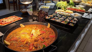 A buffet with a large pot of rice, various salads, and a pizza.