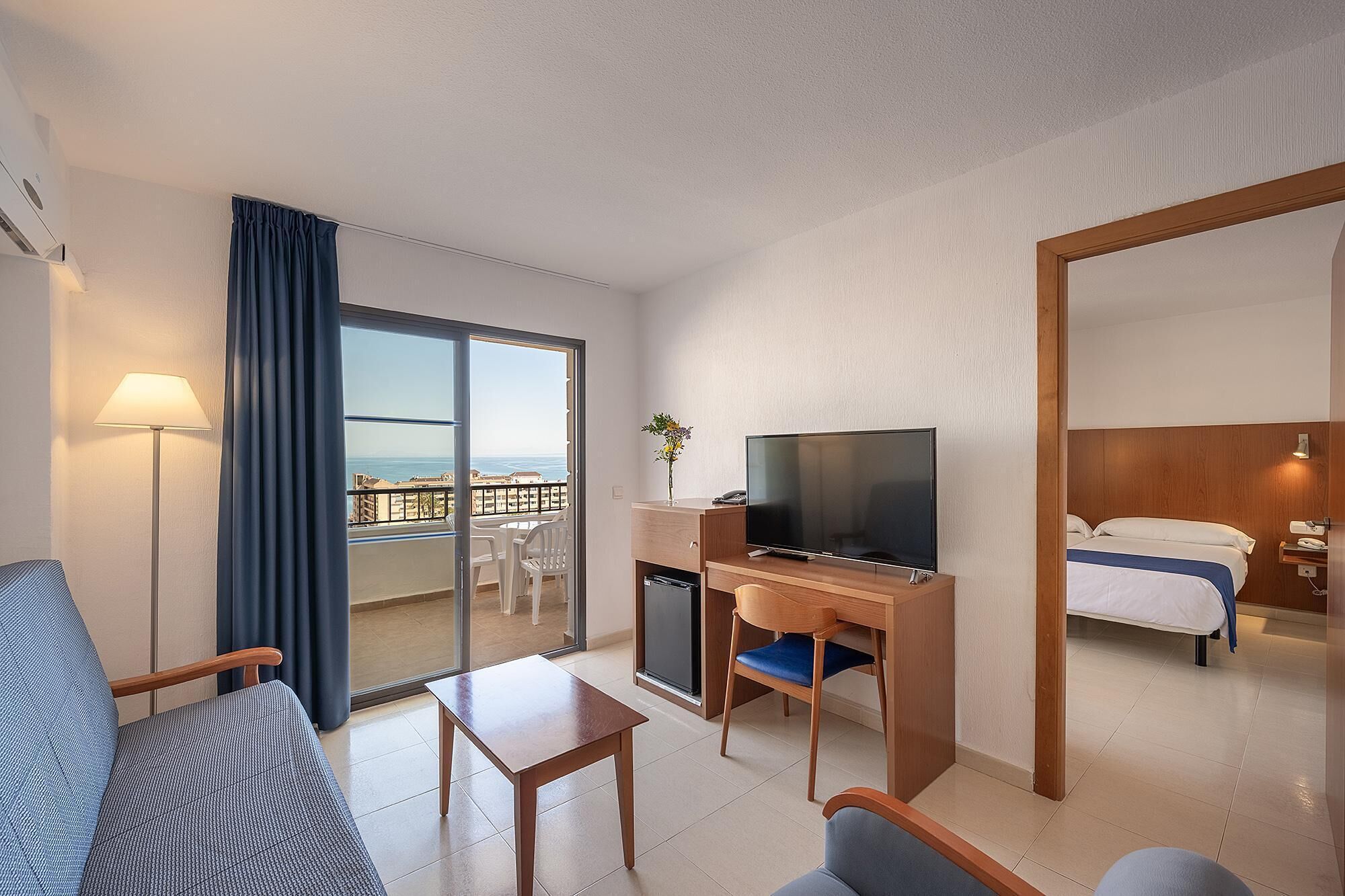 A hotel room with a balcony, a TV, a desk, a chair, and a bed.