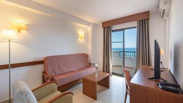 A hotel room with a sofa, two armchairs, a desk with a computer, and a view of the sea.