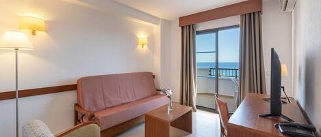 Habitación de hotel con sofá, dos sillones, un escritorio con computadora y vista al mar.