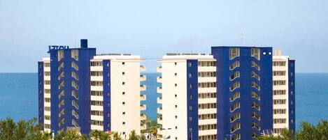 A beachfront hotel with multiple blue and white buildings, featuring balconies and a view of the sea.