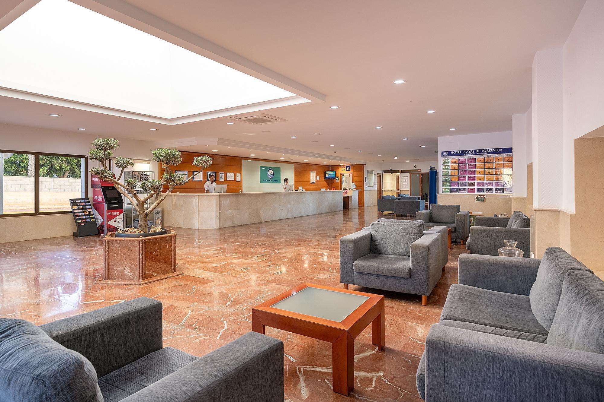 Vestíbulo de hotel con mostrador de recepción, zona de estar y un amplio ventanal.