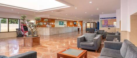Vestíbulo de hotel con mostrador de recepción, zona de estar y un amplio ventanal.