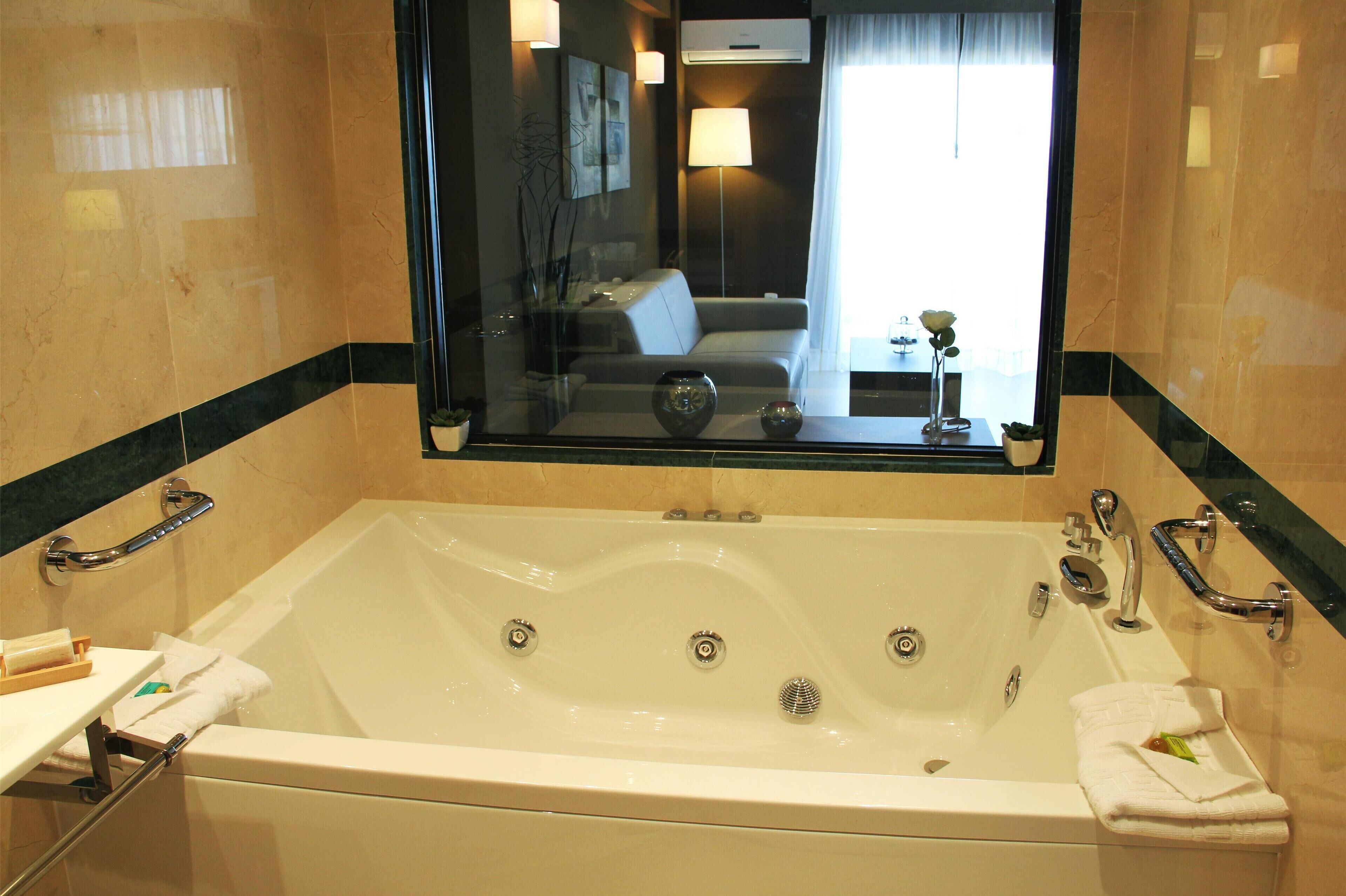 Una bañera grande y blanca con múltiples grifos y cabina de ducha con paredes de vidrio.