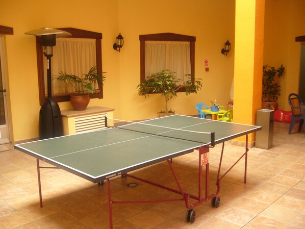 Una mesa de ping pong en una habitación con paredes amarillas, plantas en macetas y una lámpara.
